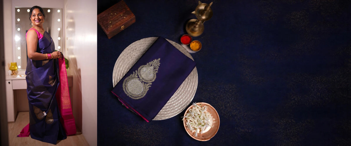 Woman wearing a navy and pink silk saree beside a folded navy saree with brass lamp
